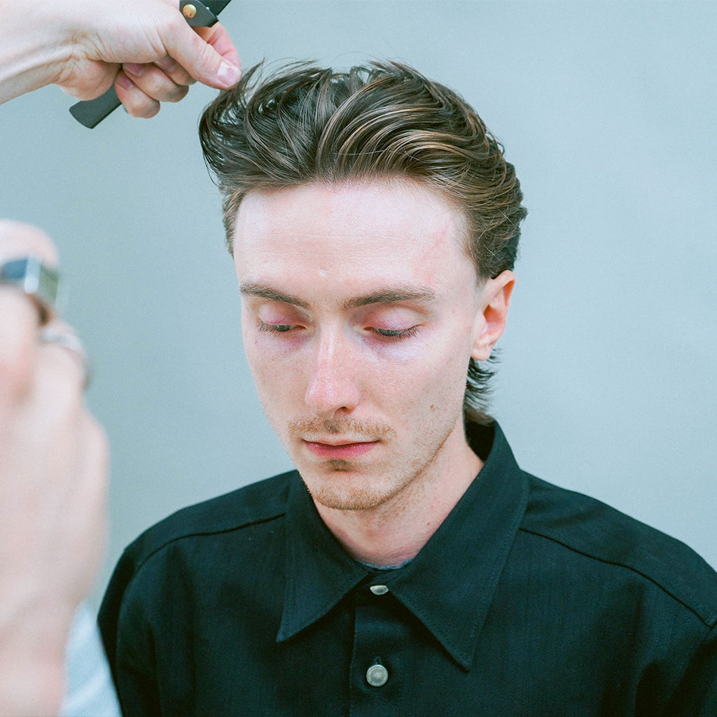 Model with chestnut color wavy hair being styled by a barber using Ceremony Wide Tooth Flip Comb