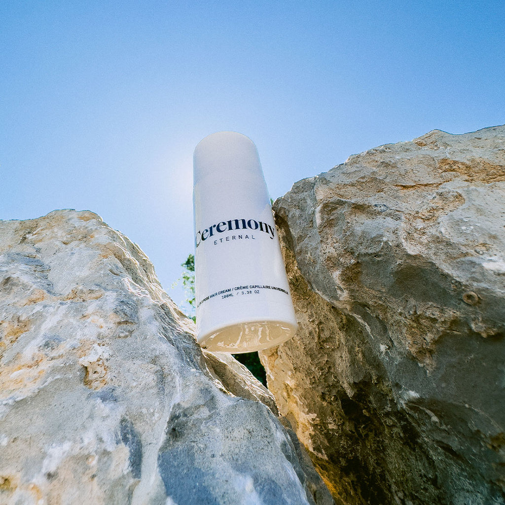 White 100 ml Pump Bottle of Ceremony Eternal All Purpose Leave-in Hair Cream in between two rocks