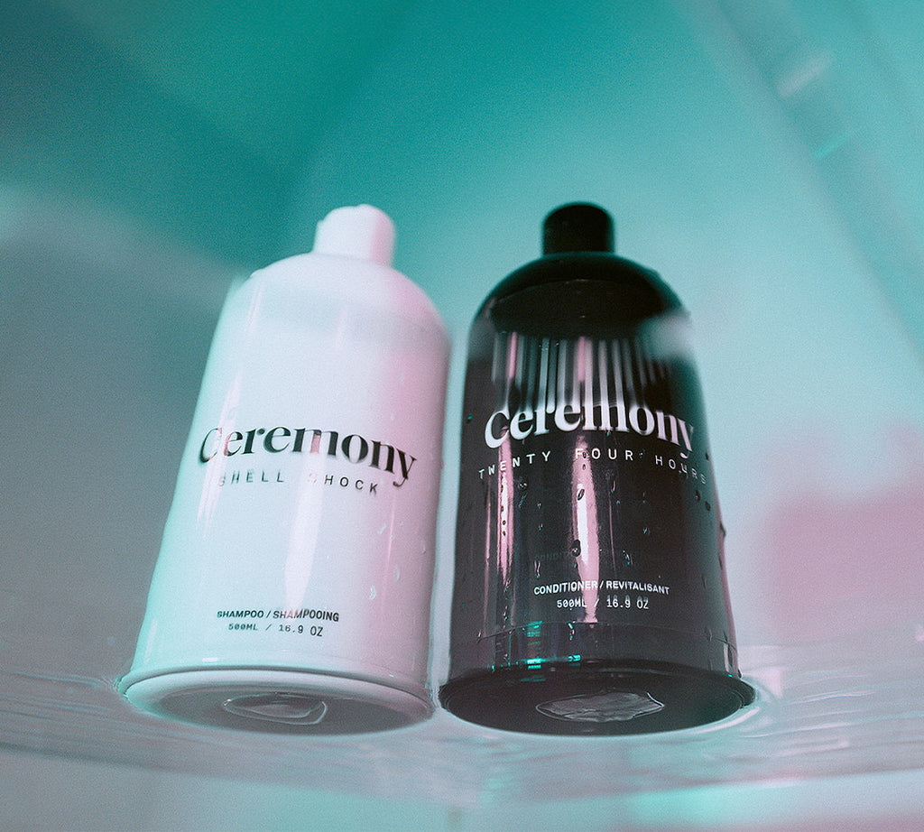 Ceremony Shell Shock shampoo 500 ml and Twenty Four Hours conditioner 500 ml bottles viewed from below with water droplets, artistic blue-toned
