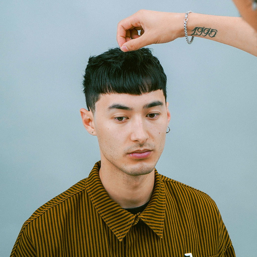 Model with dark straight crop haircut getting their hair styled by a barber
